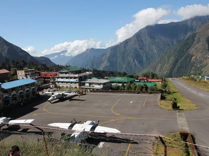 Flugzeuge stehen auf dem Rollfeld eines Flughafens, der sich inmitten einer bergigen Landschaft befindet.