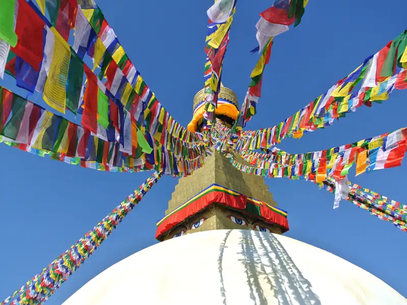 Gebetsfahnen, die im Wind über einer Stupa wehen.