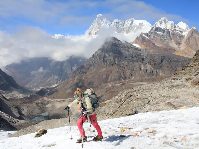 Wanderer mit Stöcken und Rucksack überquert einen verschneiten Bergpfad im Himalaya.
