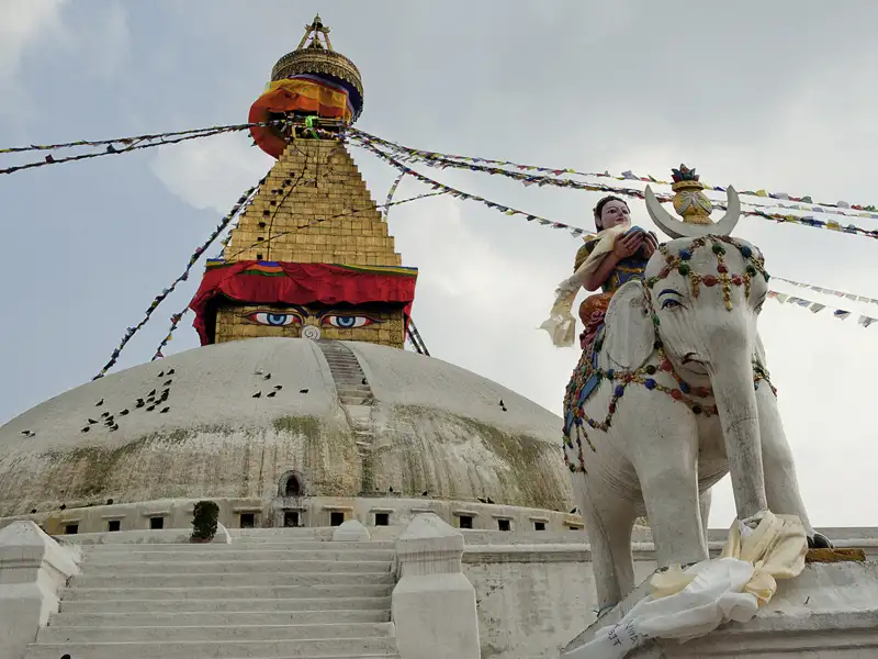 Weiße Elefantenstatue vor einer Stupa mit den Augen Buddhas.