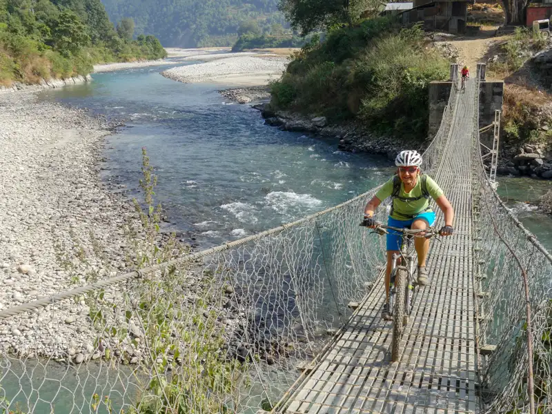 Radfahrer auf einer Hängebrücke über einen Fluss.