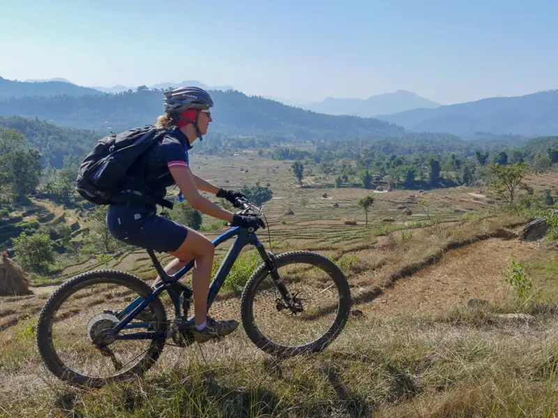 Mountainbikerin auf einem Bergpfad mit Blick auf terrassierte Felder.