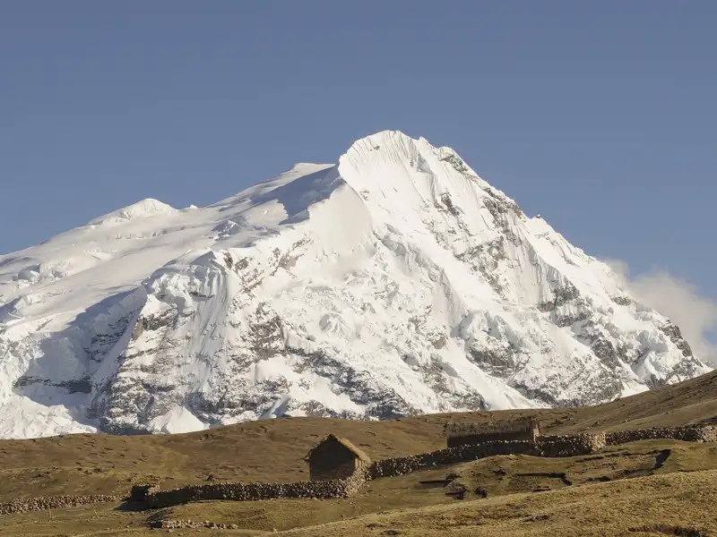 Schneebedeckter Berggipfel in den Anden mit einer kleinen Hütte und Steinmauern im Vordergrund.