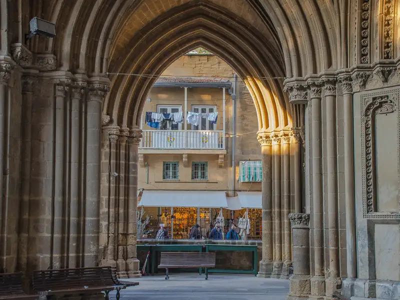 Blick durch einen Torbogen auf einen Marktstand und ein Wohnhaus mit Wäsche auf dem Balkon.