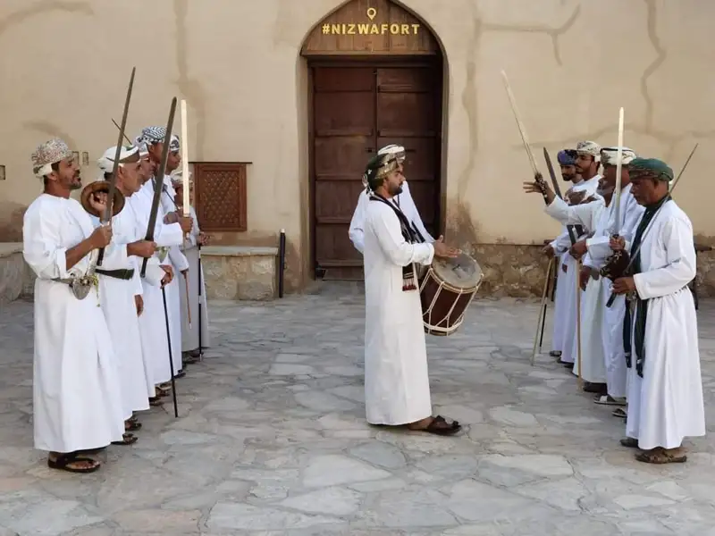 Omanische Männer in traditioneller Kleidung führen einen Schwerttanz und spielen Trommel vor dem Nizwa Fort.