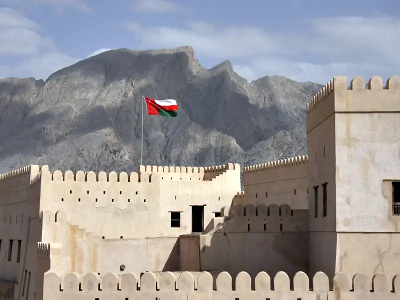 Historisches omanisches Fort mit wehender Flagge und Gebirgslandschaft im Hintergrund.