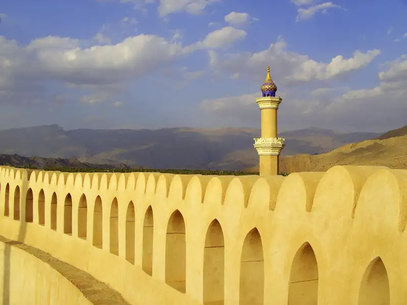 Festungsmauer mit Minarett und Berglandschaft im Hintergrund.