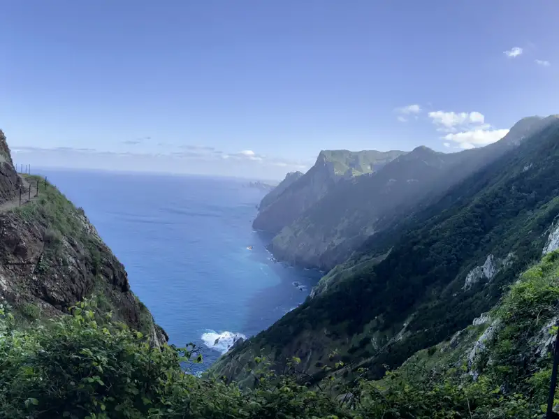 Wanderweg entlang der Küste mit Blick auf das blaue Meer und die bewachsenen Klippen.
