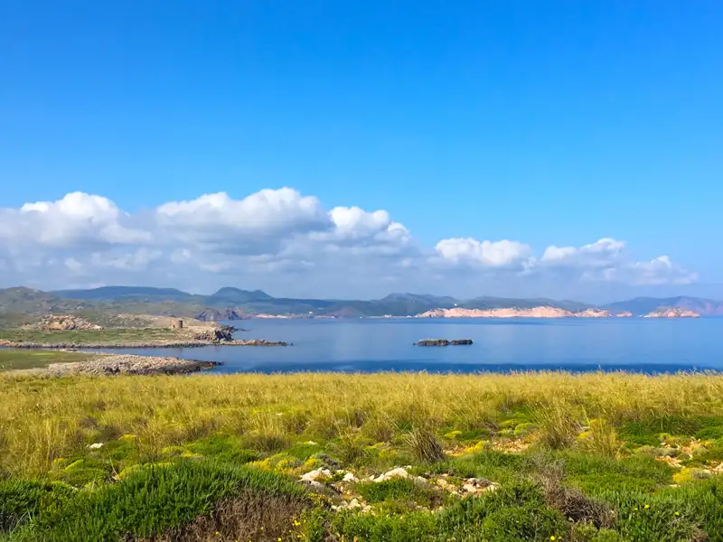 Blick auf die Küste mit Hügeln im Hintergrund und einem alten Turm am Ufer.