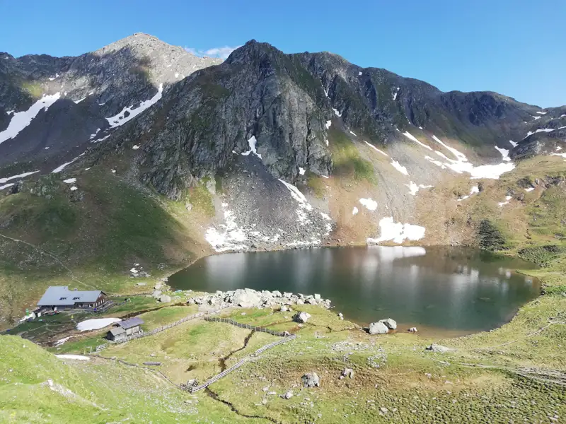 Alpenpanorama mit Bergsee und Hütte.