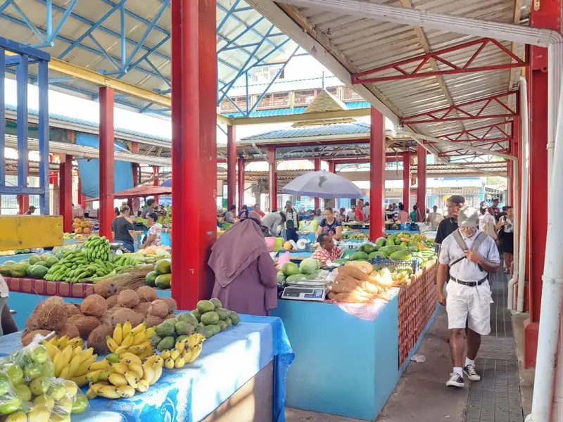 Marktstände mit tropischen Früchten und Gemüse, besucht von Einheimischen.