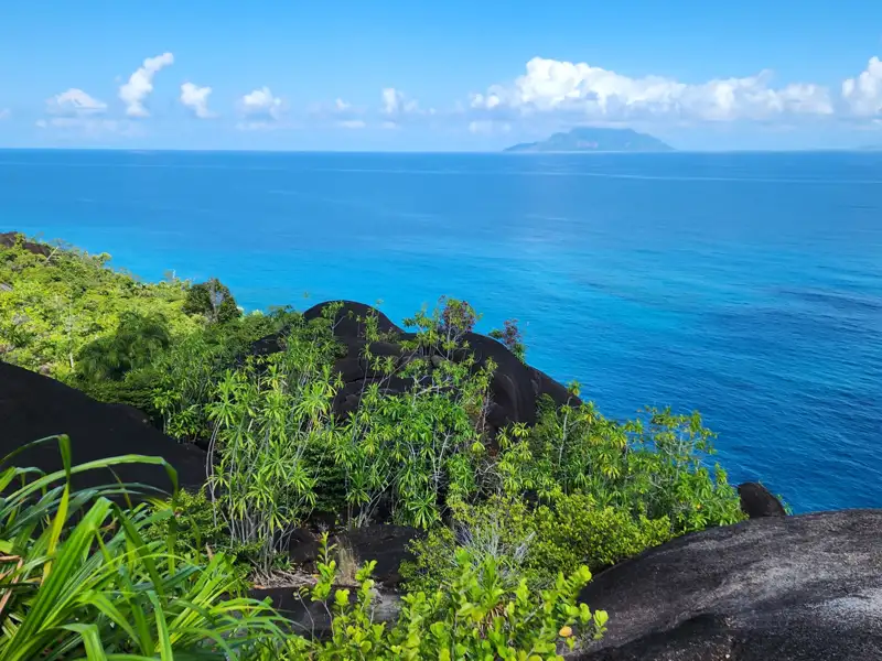Blick vom Küstenpfad auf das türkisfarbene Meer und eine Insel am Horizont.