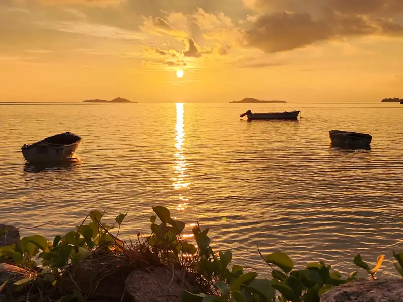 Sonnenuntergang über dem Meer mit drei Booten im Vordergrund.