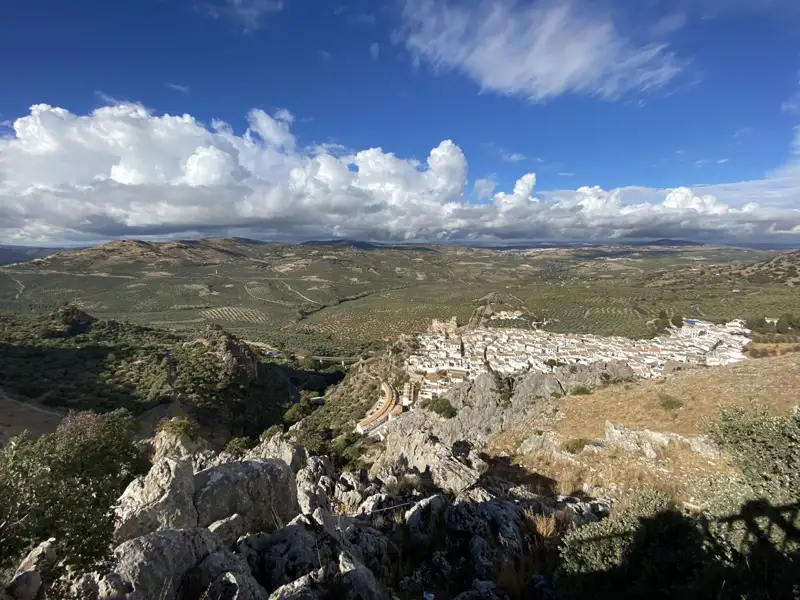Panoramablick auf ein weißes Dorf in einer hügeligen Landschaft mit Feldern und Vegetation.