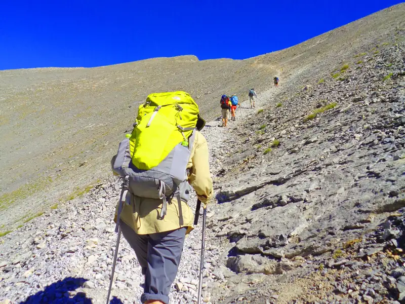 Wanderer mit Rucksäcken auf einem steinigen Bergpfad.