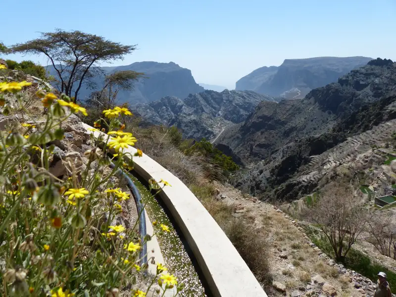 Blick auf die terrassierten Felder und das Gebirge, entlang eines Bewässerungskanals.