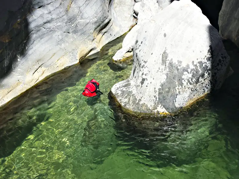 Eine rote Schwimmhilfe treibt in einem smaragdgrünen Flussbecken, das von Felsen umgeben ist.