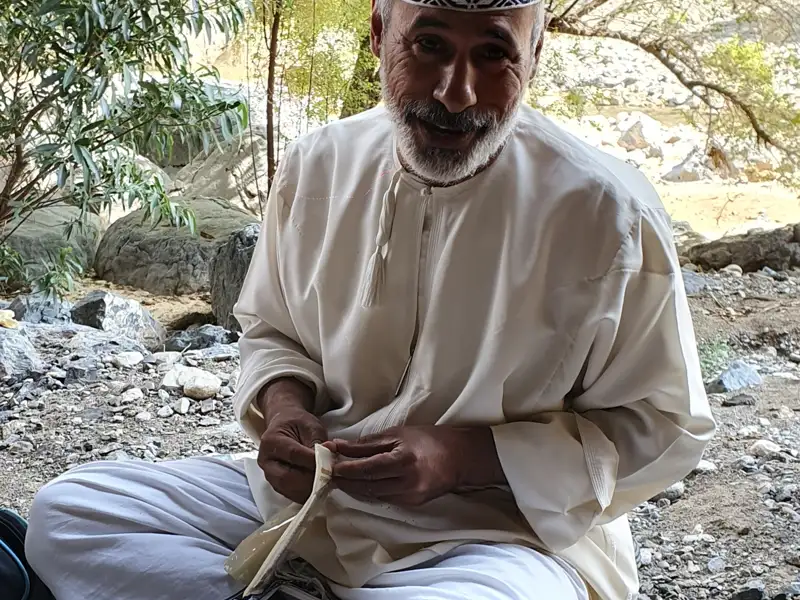 Ein Mann in traditioneller Kleidung bearbeitet Stoff am Flussufer.