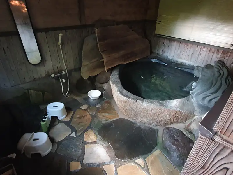 Traditionelles Onsen mit Steinwanne und Duscharmatur.