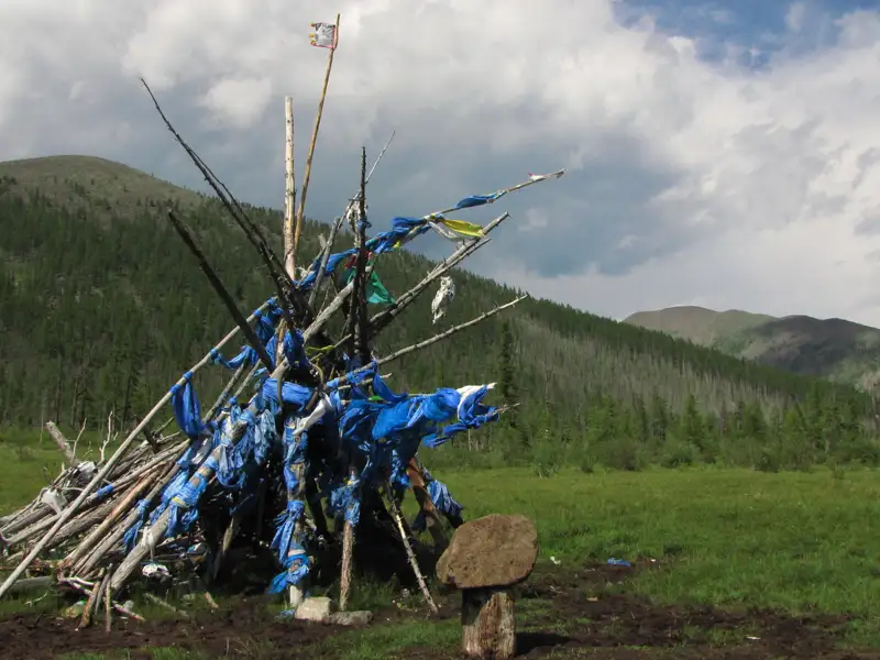 Gebetsstätte mit blauen Gebetsfahnen und einem Stein in der Vordergrund, im Hintergrund eine bewaldete Berglandschaft.