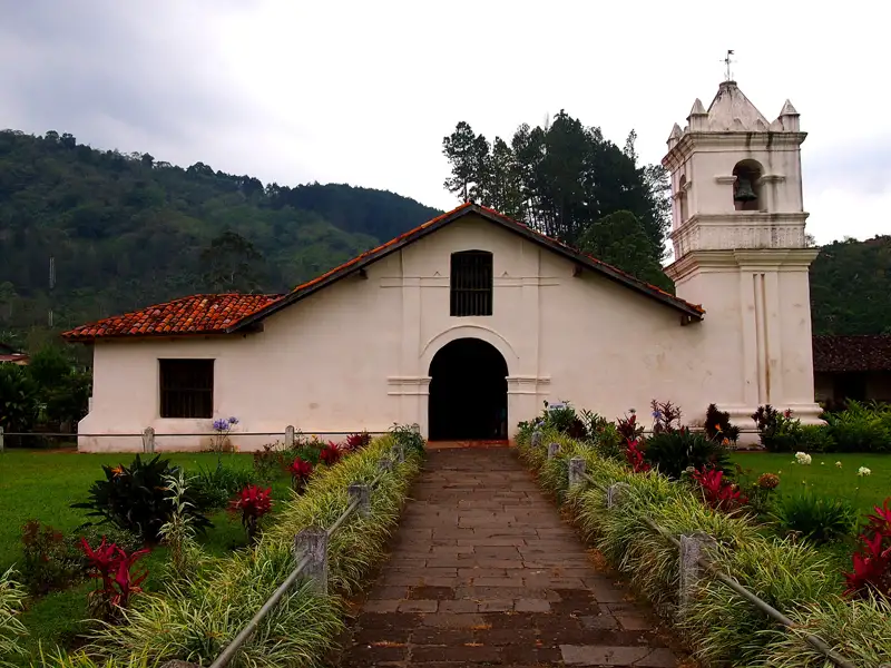 Historische Kirche mit Ziegeldach und Glockenturm inmitten einer grünen Landschaft.