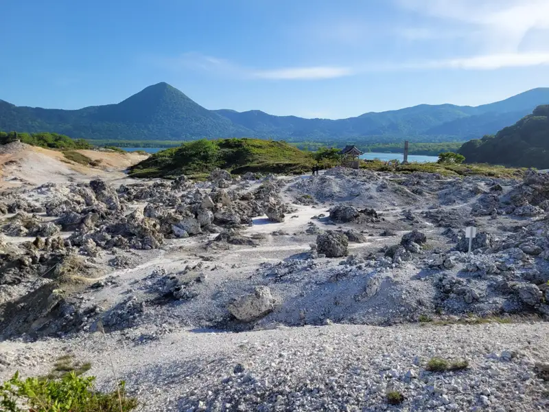 Vulkanische Gesteinsformationen mit Bergen und See im Hintergrund.
