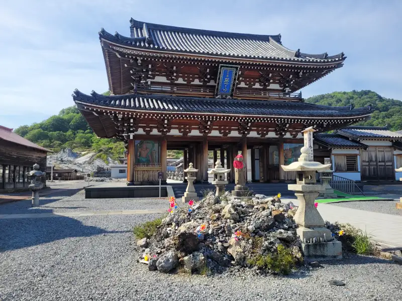 Eingangstor eines japanischen Tempels mit traditionellen Steinlaternen und einem Steinhaufen im Vordergrund.