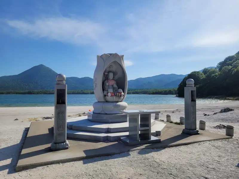 Statue am Seeufer mit Bergkulisse.