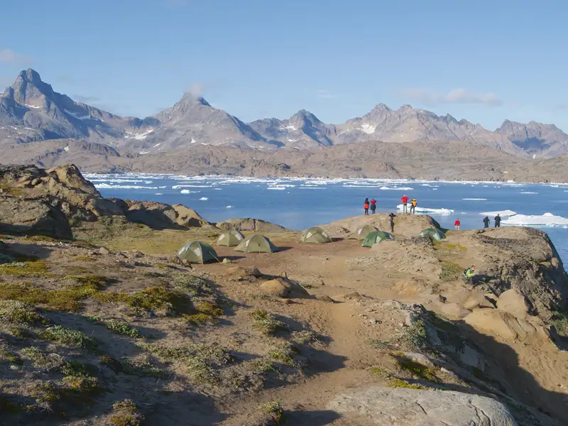 Campingplatz in einer arktischen Landschaft mit Zelten, Eisbergen und Bergen im Hintergrund.