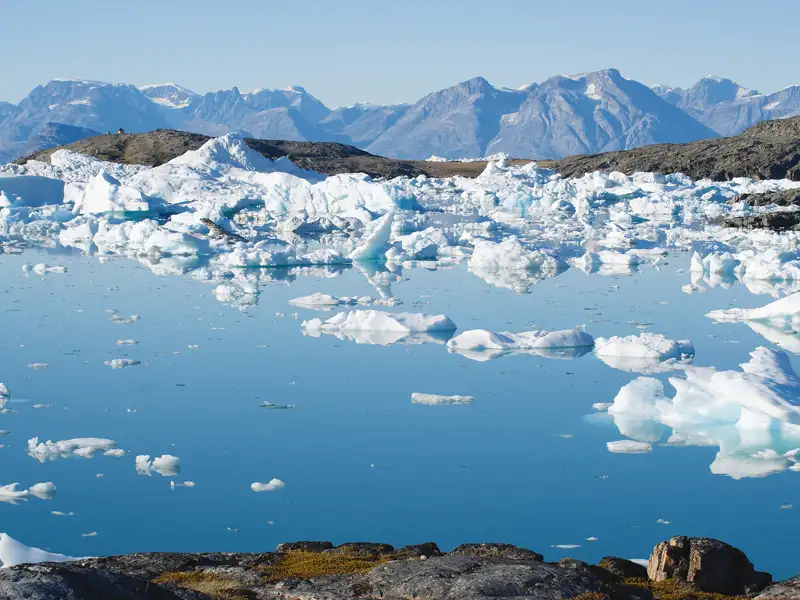 Wanderer mit Blick auf einen Eisberg in der grönländischen Landschaft.