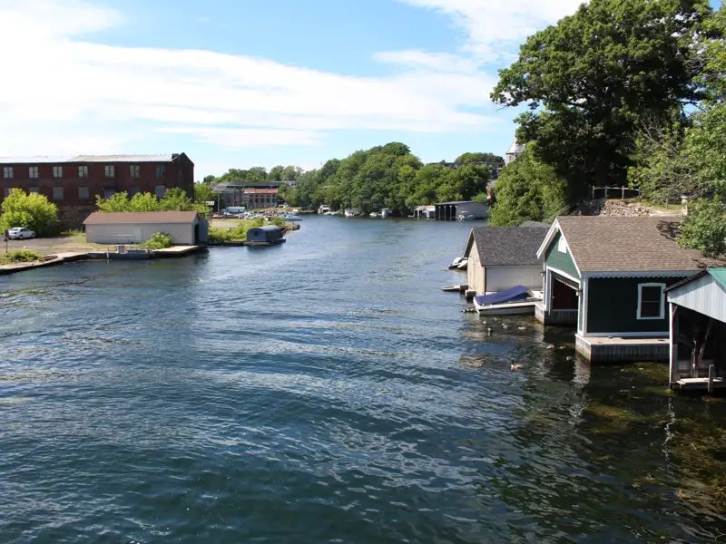 Bootshäuser am Flussufer mit Gebäuden im Hintergrund.