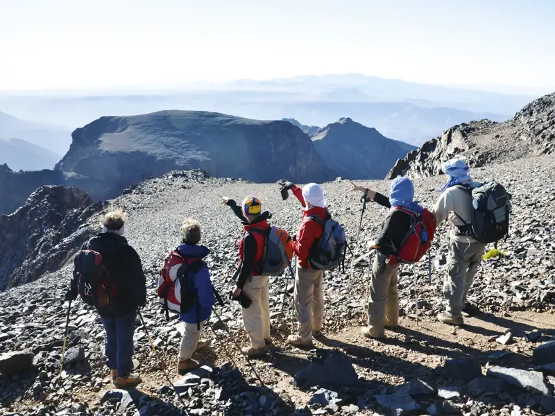 Wanderer mit Rucksäcken und Wanderstöcken betrachten die Berglandschaft von einem Gipfel aus.