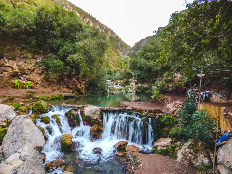 Ein Wasserfall in einer bewaldeten Schlucht mit Sitzgelegenheiten am Ufer.
