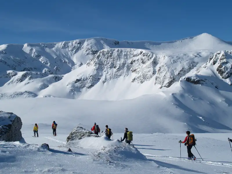 Skitourengeher durchqueren eine verschneite Berglandschaft.