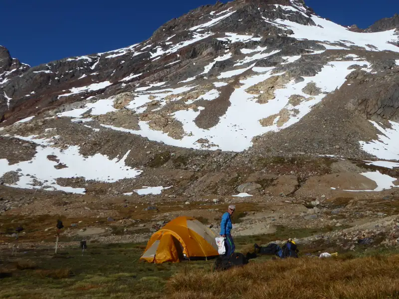 Wanderer im Basislager mit Zelt vor schneebedecktem Berg