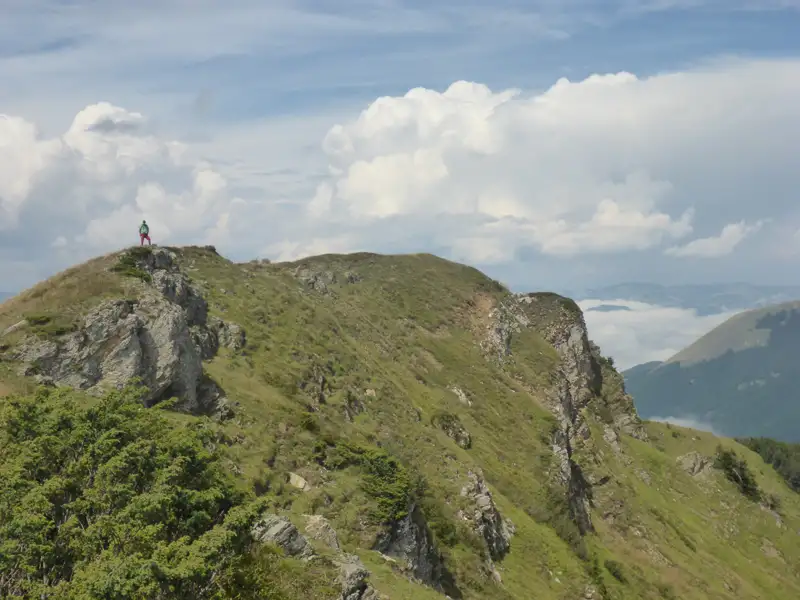 Wanderer auf einem Berggipfel mit Blick auf die umliegenden Berge und Täler.