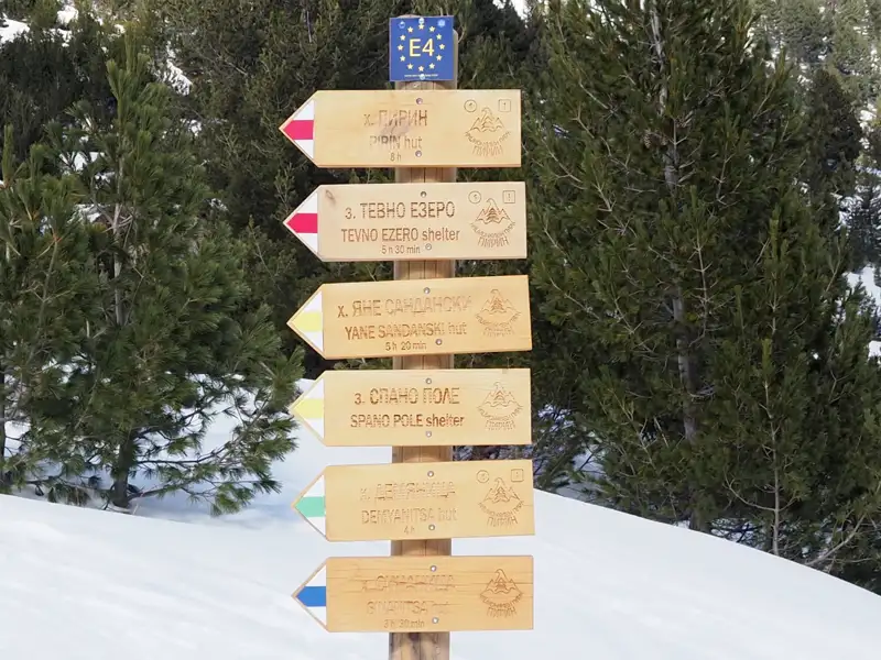 Wegweiser im Pirin-Gebirge mit Angaben zu Wanderwegen und Hütten, inklusive Gehzeiten und E4-Symbol.