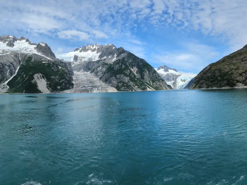 Panoramablick auf einen Gletscher, der in einen türkisfarbenen See mündet, umgeben von schneebedeckten Bergen.