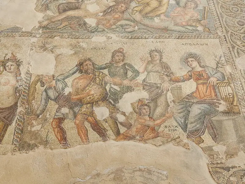 Abgebildetes Detail eines römischen Mosaiks mit verschiedenen Figuren, möglicherweise aus der Mythologie, und griechischen Inschriften.