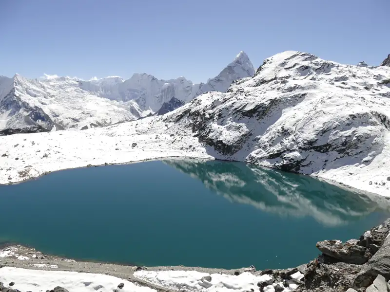 Türkisfarbener See inmitten schneebedeckter Berge.