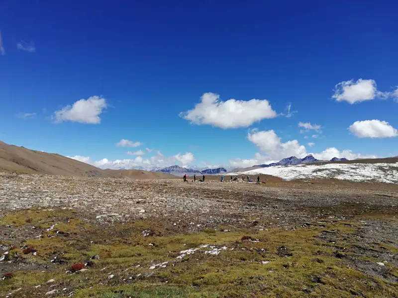Wanderer in einer hochgelegenen Landschaft mit schneebedeckten Bergen im Hintergrund.