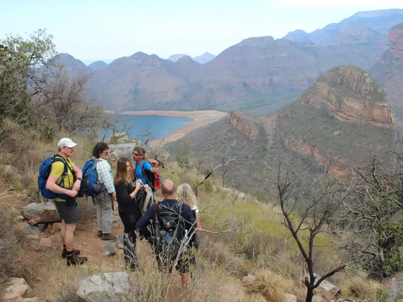 Wandergruppe pausiert auf einem Bergpfad und betrachtet die Landschaft mit Schlucht und Stausee.