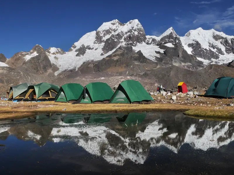 Basislager in den Bergen mit Zelten und einem kleinen See.