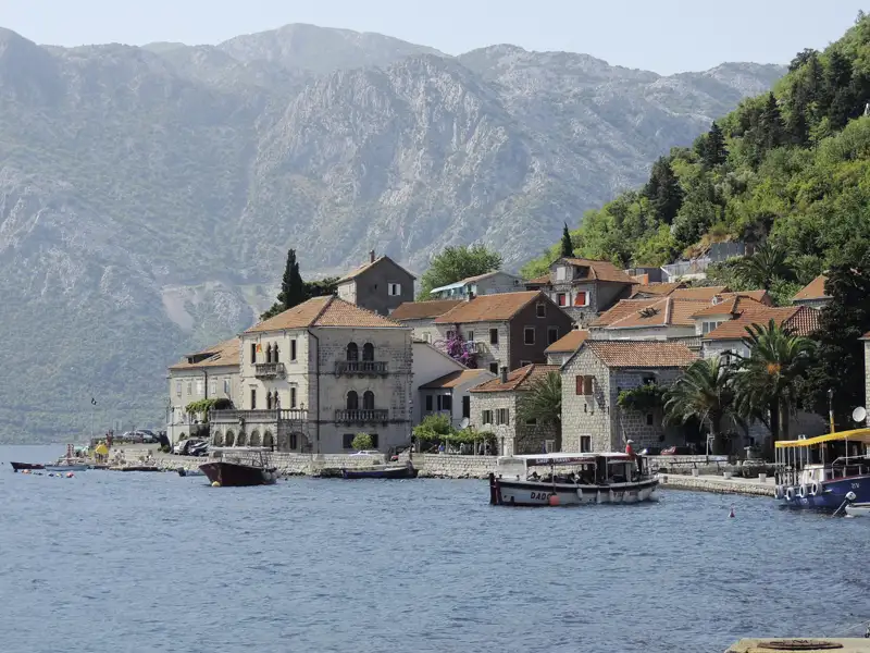Montenegrinische Küstenstadt mit traditionellen Häusern und Booten im Hafen.