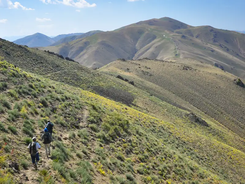 Wanderer auf einem Bergpfad in hügeligem Gelände.