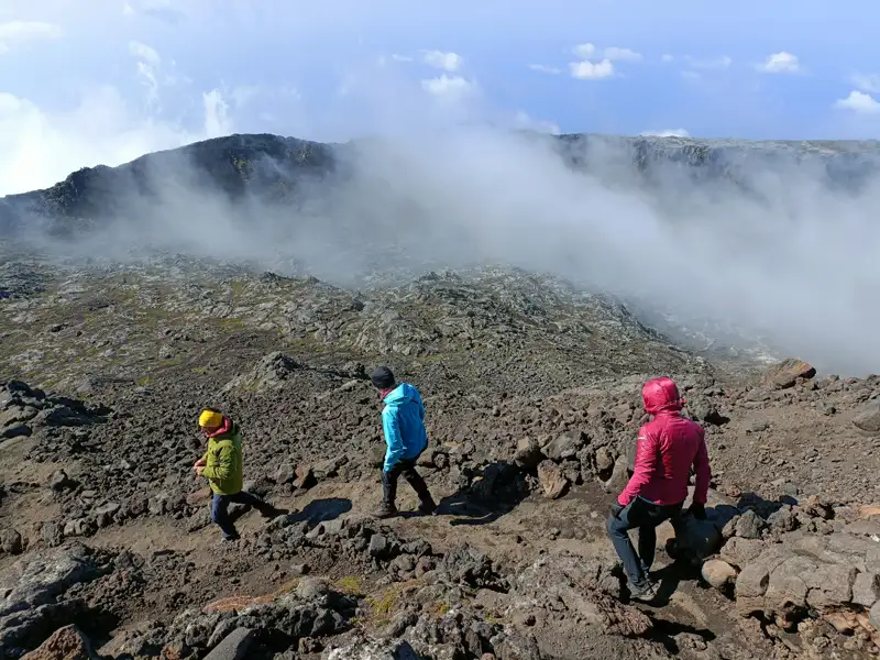Wanderer auf einem vulkanischen Pfad. Nebel bedeckt den Gipfel des Vulkans im Hintergrund.