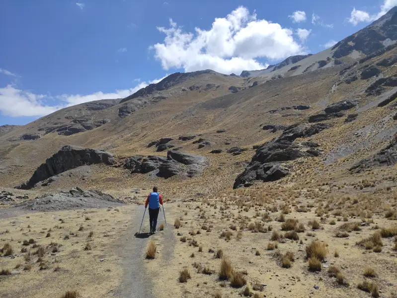 Wanderer mit Wanderstöcken auf einem Bergpfad in einer kargen Landschaft.