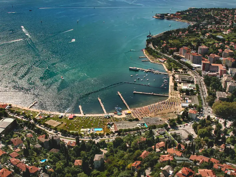 Luftaufnahme des Küstenabschnitts mit Strand, Hafen und umliegenden Gebäuden.