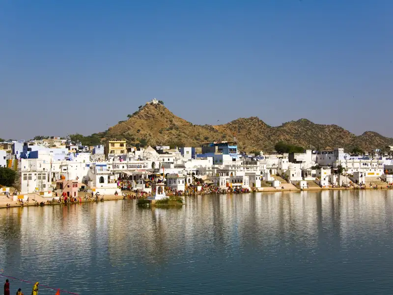Heiliger See in Pushkar mit den umliegenden Gebäuden und Hügeln im Hintergrund.