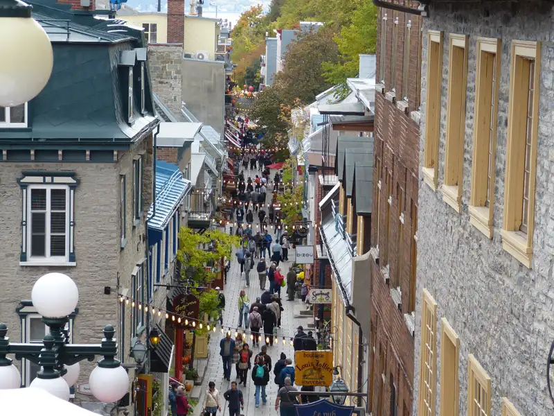 Belebte Fußgängerzone in Quebec City mit historischen Gebäuden und vielen Menschen.